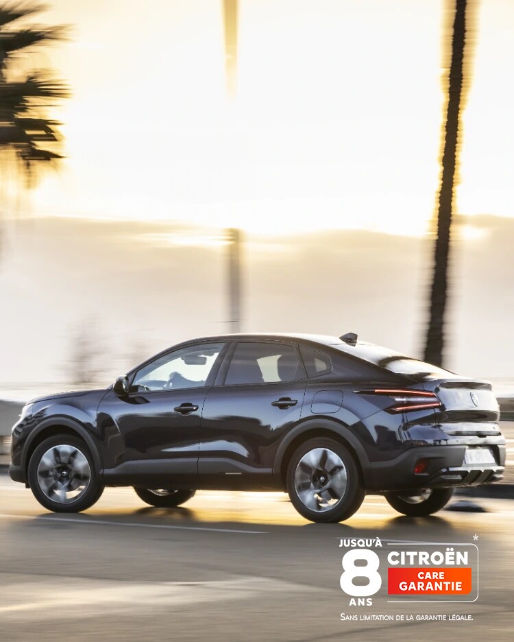 Citroën ë-C4 X roulant sur une route côtière au coucher du soleil, arborant le badge de couverture Citroën sur 8 ans