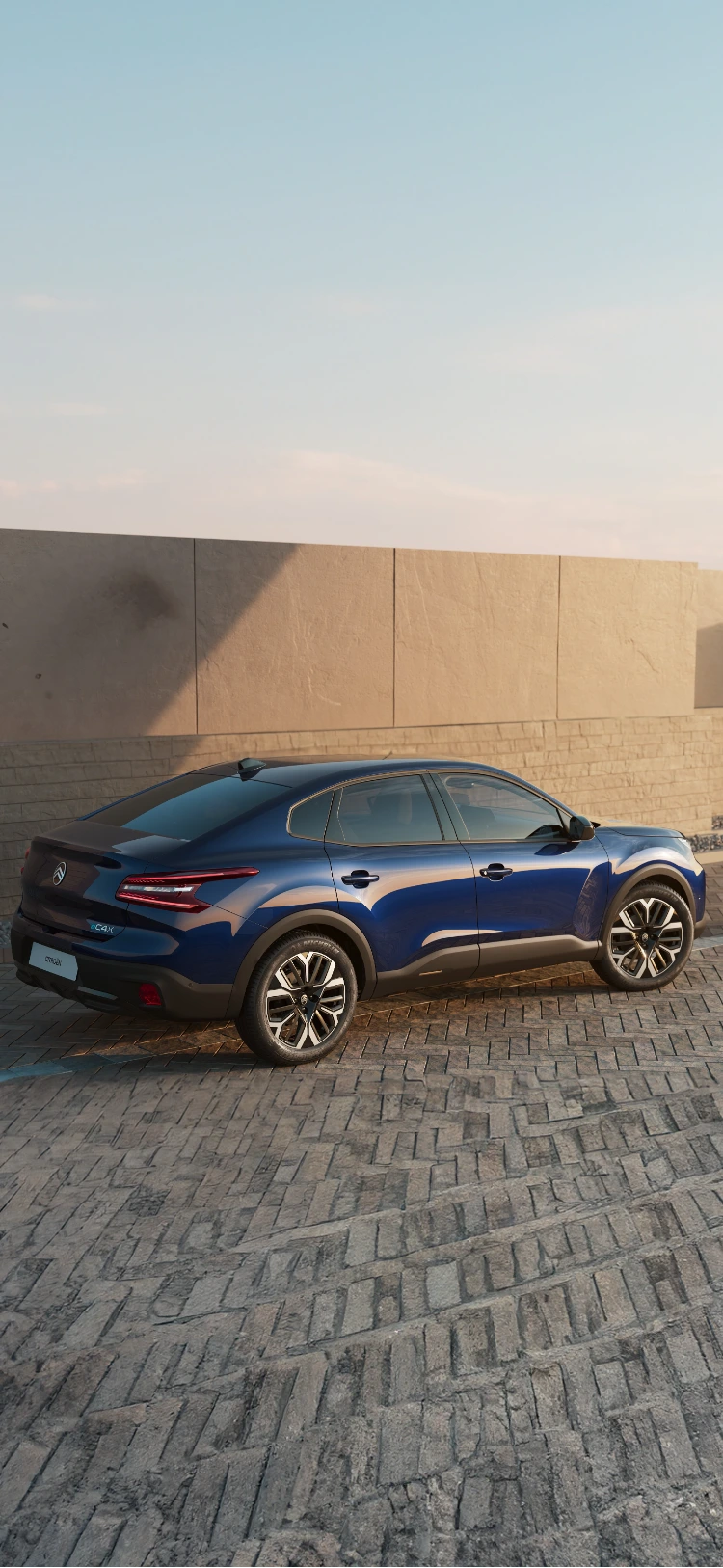 Vue latérale de la Citroën C4 X roulant le long de la côte au coucher du soleil, mettant en valeur son profil élégant